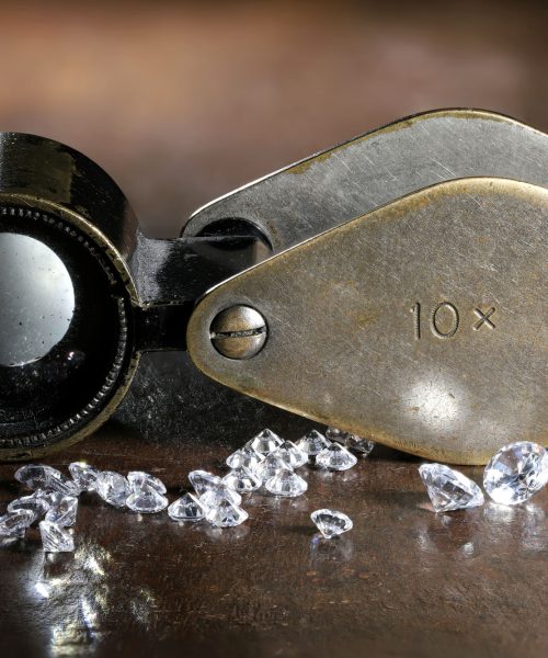 brilliant cut diamonds with folding magnifier on wooden backgrou